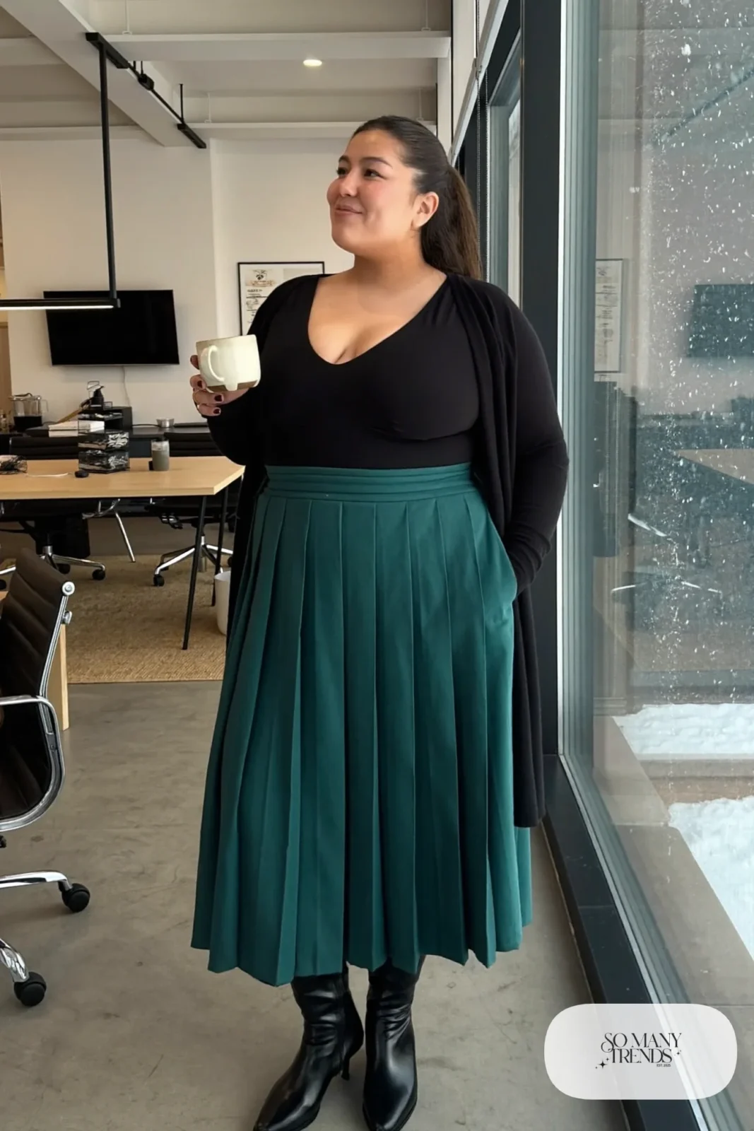 Woman in teal pleated midi skirt, black V-neck top, long black cardigan and black boots, outfit 26