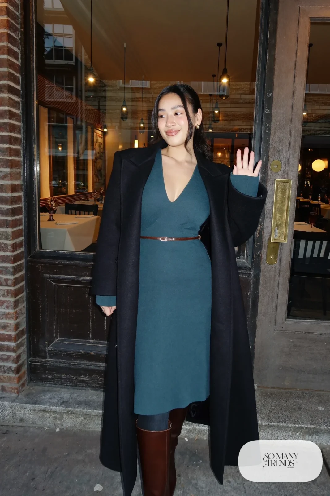 Woman in teal knit V-neck midi dress with espresso belt, long black coat and brown boots, outfit 32