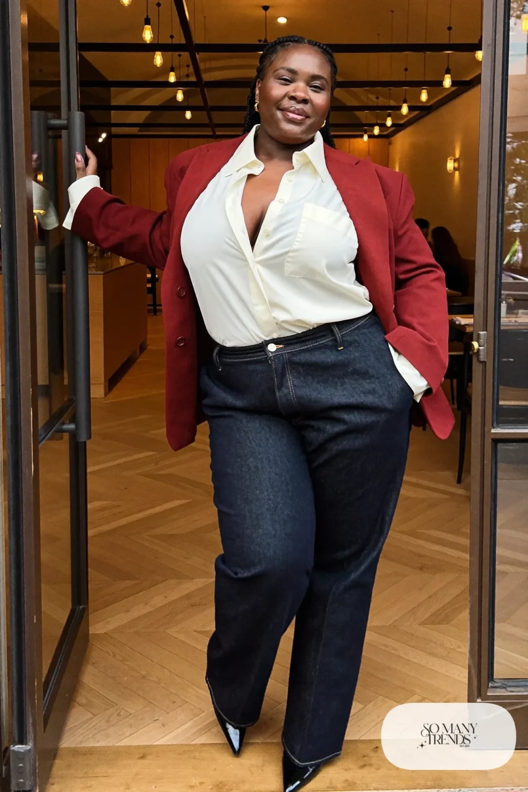 Plus size woman in dark straight jeans, ivory draped blouse, oxblood blazer and black pointed ankle boots, outfit 13