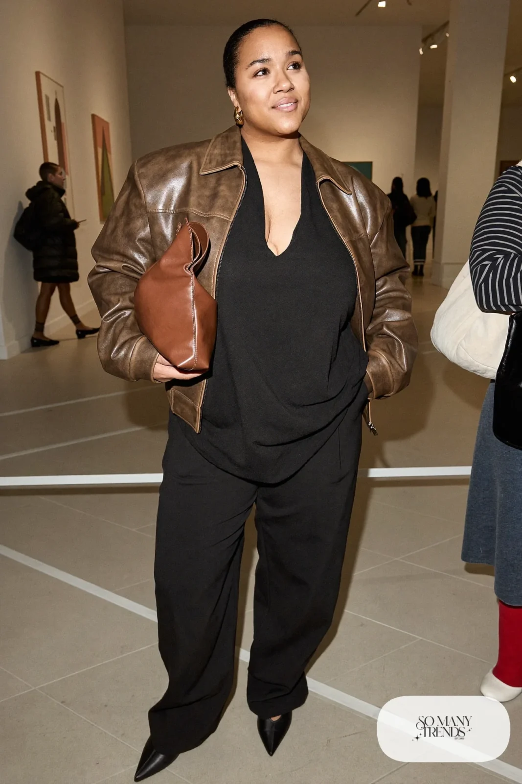 Plus size woman in brown leather bomber, black top, black wide pants and black closed flats, outfit 17