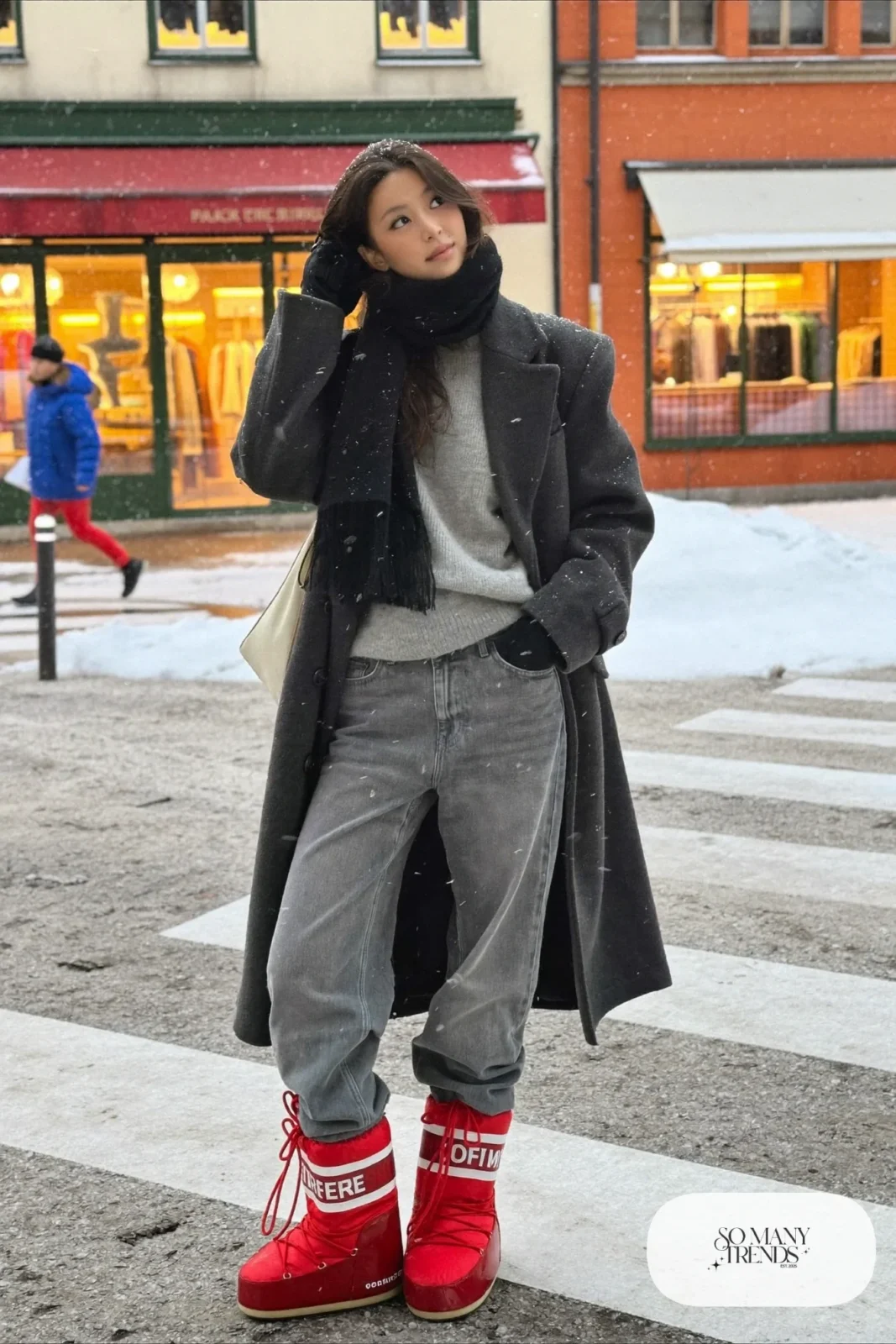 Woman in charcoal long wool coat, gray straight jeans and cherry red moon boots on a snowy sidewalk, outfit 2