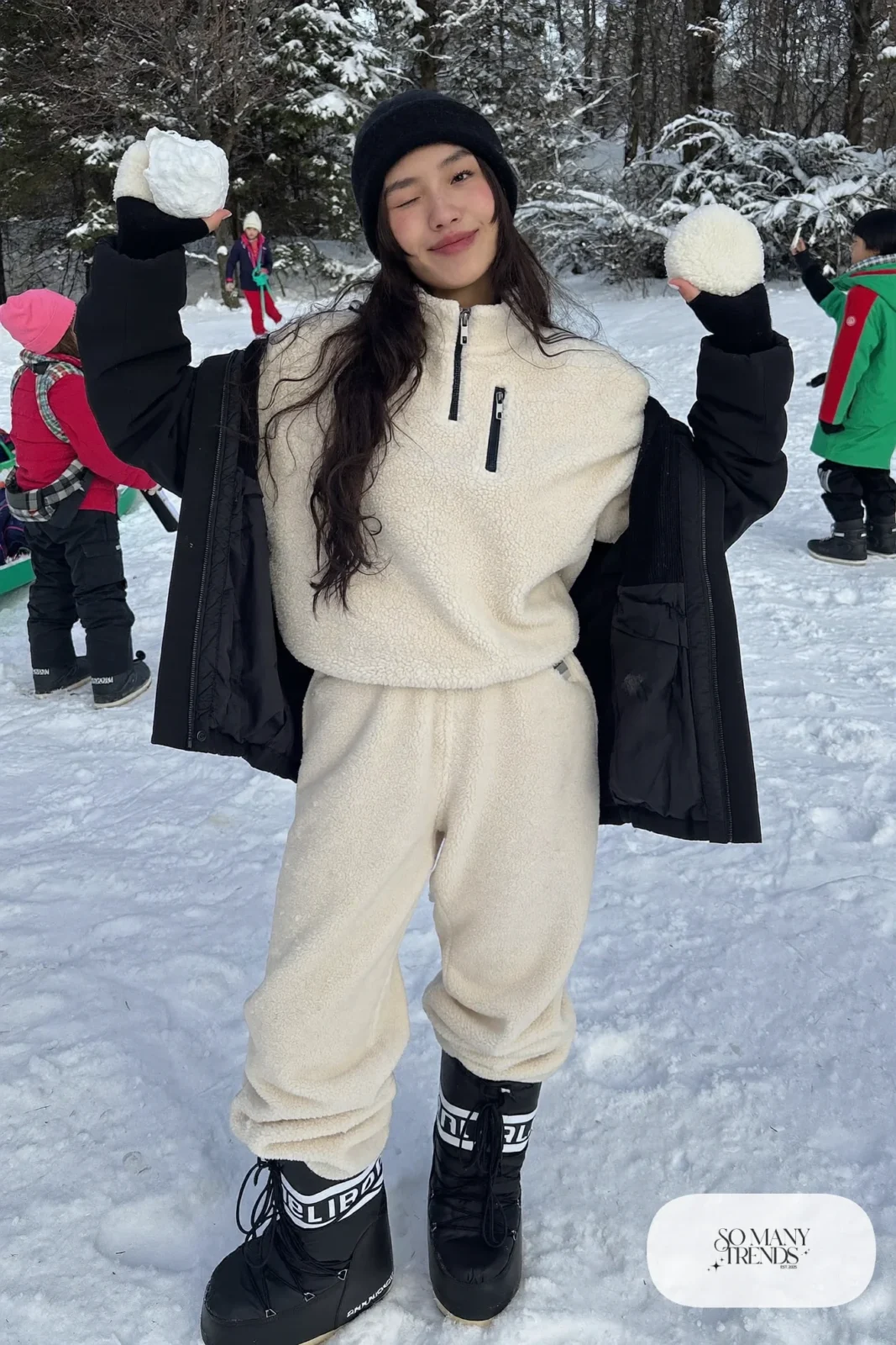 Woman in cream teddy fleece pullover, straight fleece pants, black moon boots and a black shell jacket in the snow, outfit 3