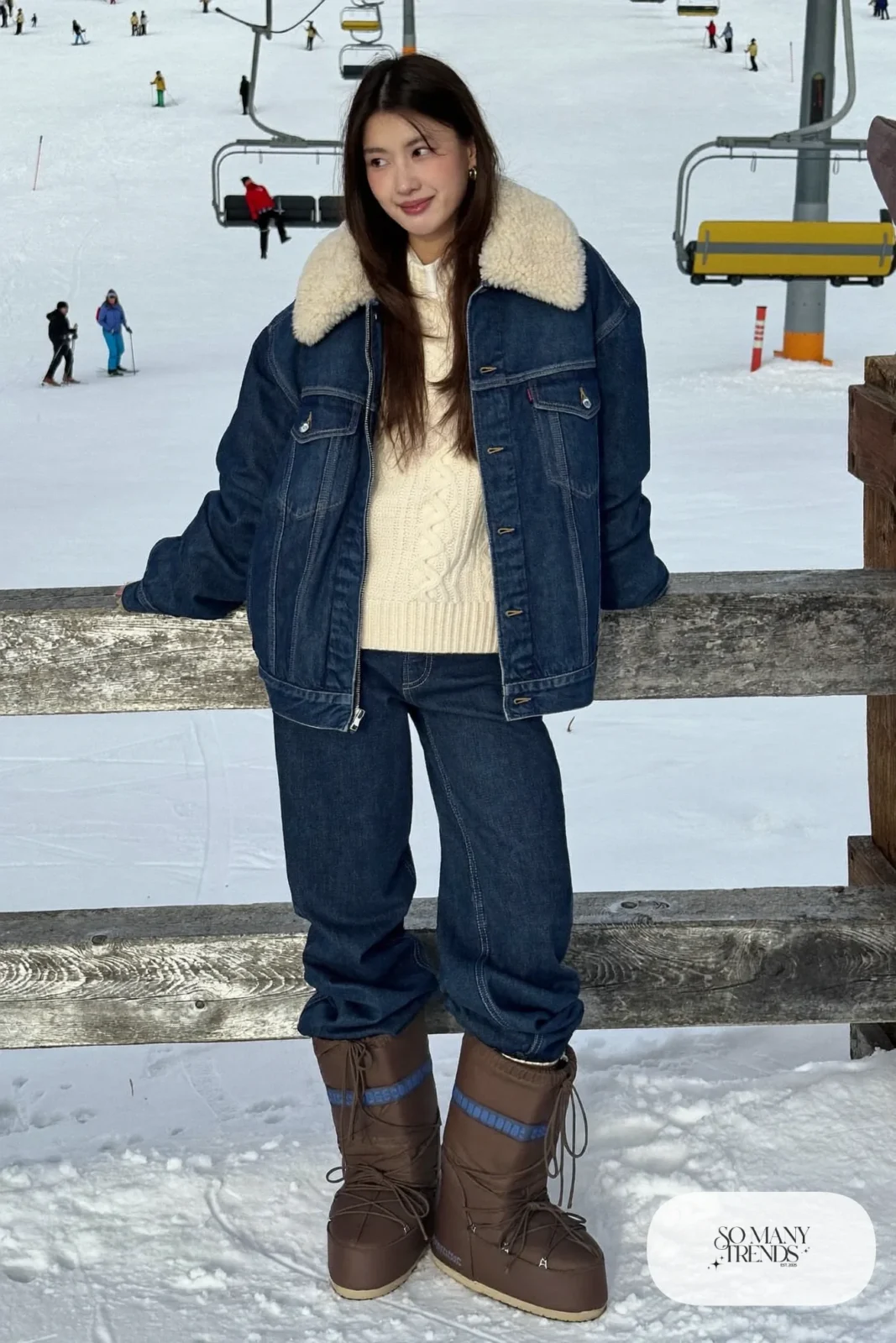 Woman in sherpa-lined indigo denim jacket, cream chunky sweater, straight indigo jeans and brown moon boots, outfit 4