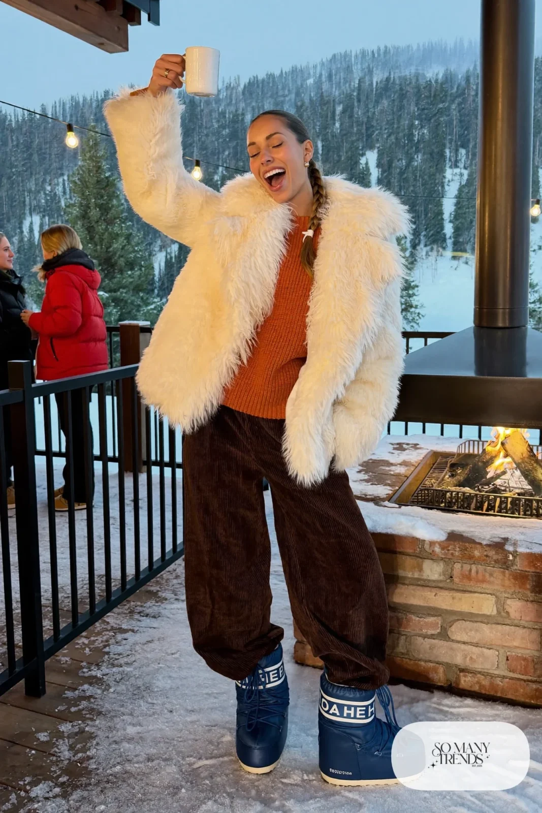 Woman in cream shearling jacket, chocolate corduroy pants, indigo moon boots and a knit sweater at an apres ski lodge, outfit 13
