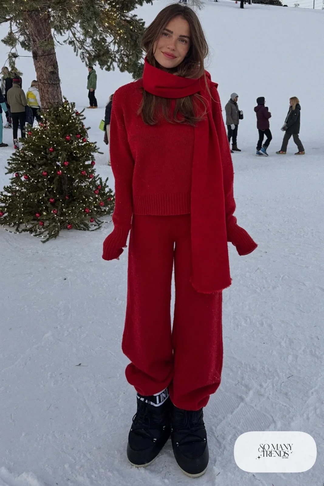 Woman in red ribbed knit sweater and matching wide-leg knit pants with black moon boots and a red scarf in the snow, outfit 15