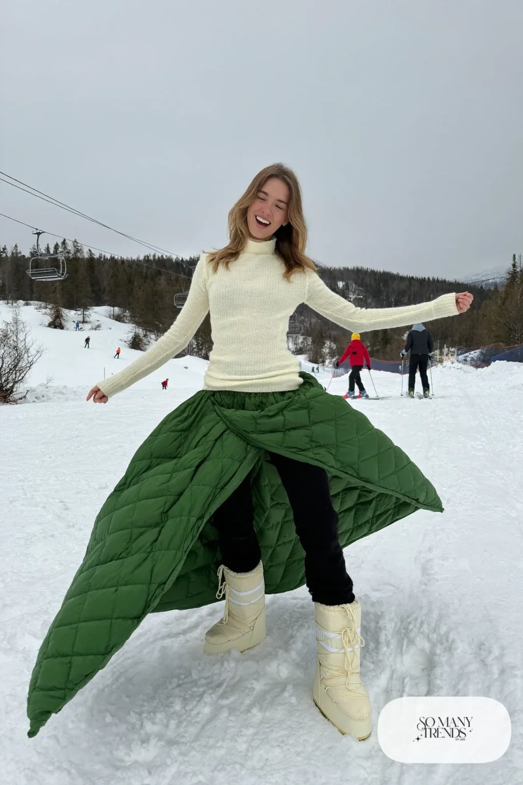 Woman in forest green quilted maxi skirt, cream fitted knit, black fleece tights and cream moon boots in the snow, outfit 18