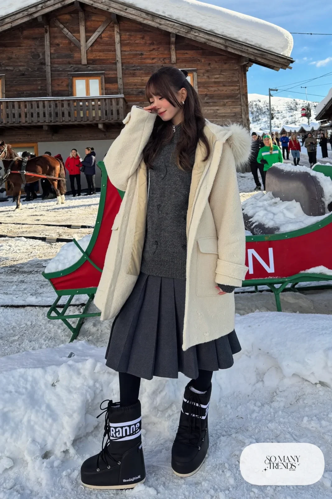 Woman in cream hooded parka, indigo pleated midi skirt, black tights and black moon boots in a snowy street, outfit 19