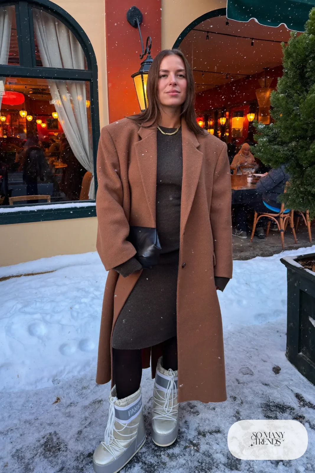 Woman in charcoal knit midi dress, long camel coat, black tights and silver moon boots in a snowy evening, outfit 20