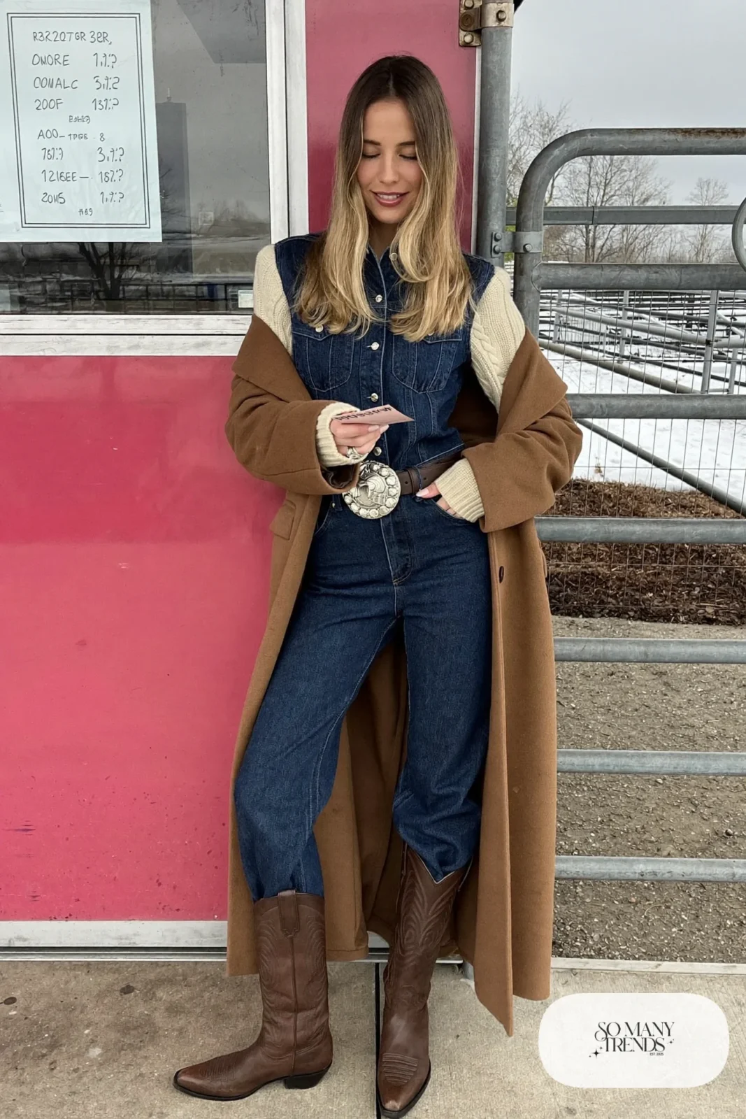 Dark denim jumpsuit with silver concho belt over cream long-sleeve knit, tall brown boots and wool coat, outfit 10