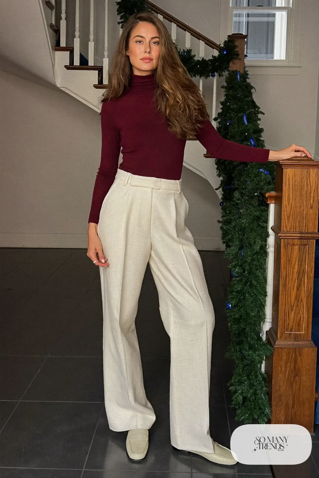 Woman in a wine fine-knit turtleneck, cream wide-leg wool pants and cream loafers in a decorated hallway, outfit 9