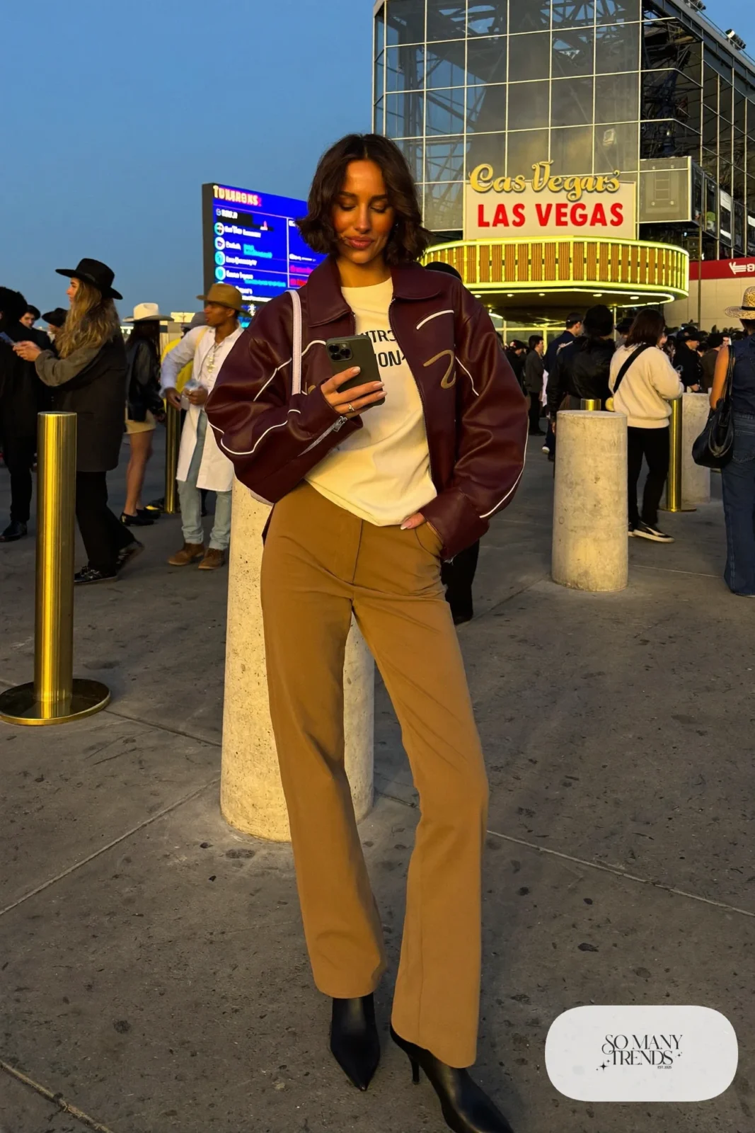 Woman in burgundy leather jacket, cream tee, camel straight pants and black boots, NFR outfit 7