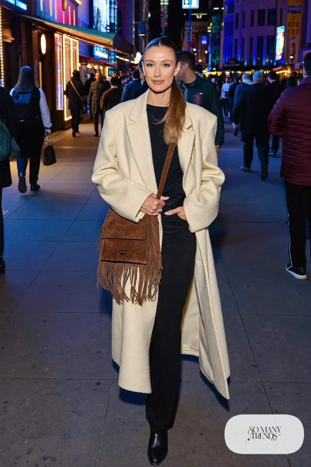 Woman in long cream coat, black sweater, black pants, chocolate fringe bag and black boots, NFR outfit 22