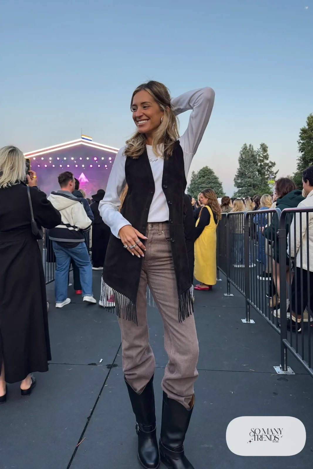 Woman in long black fringe vest, white tee, taupe jeans and black boots, outfit 19