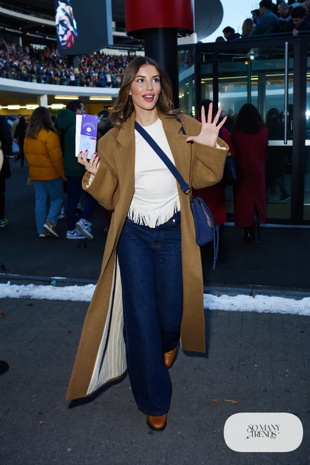 Woman in a long camel coat, white fringe-hem top, dark wide-leg jeans and cognac boots, concert outfit 14