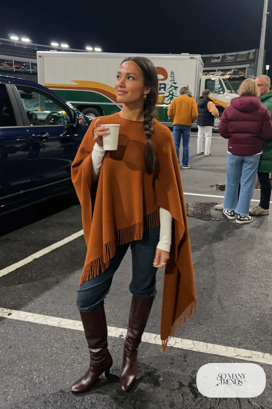 Woman in a cognac wool poncho, white tee, dark straight jeans and tall brown boots, concert outfit 16
