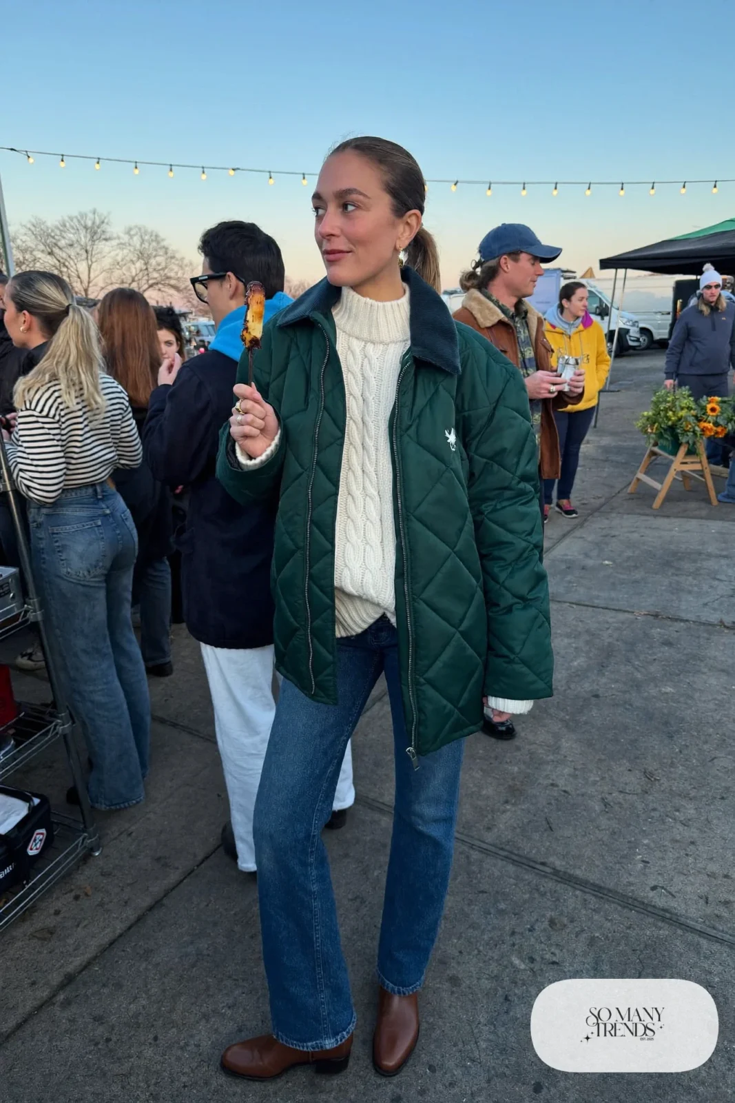 Woman in a forest green quilted jacket, cream cable sweater, straight jeans and brown boots, concert outfit 17