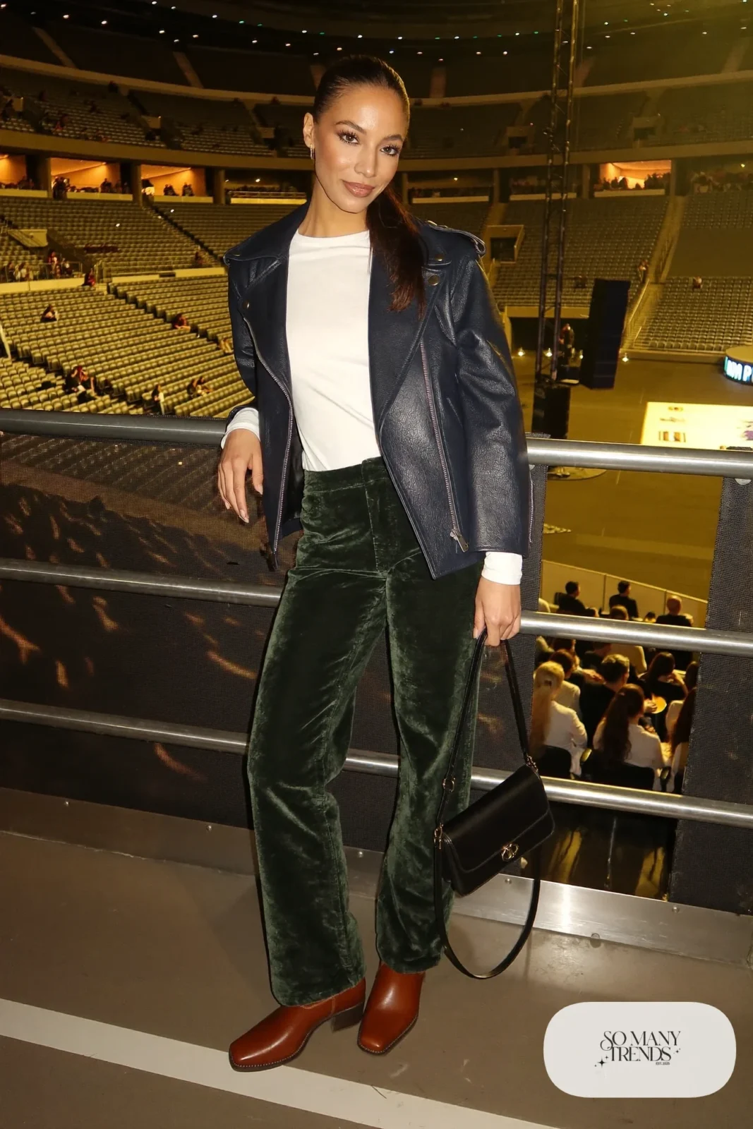 Woman in a navy moto jacket, green velvet straight pants, white tee and cognac boots, concert outfit 23