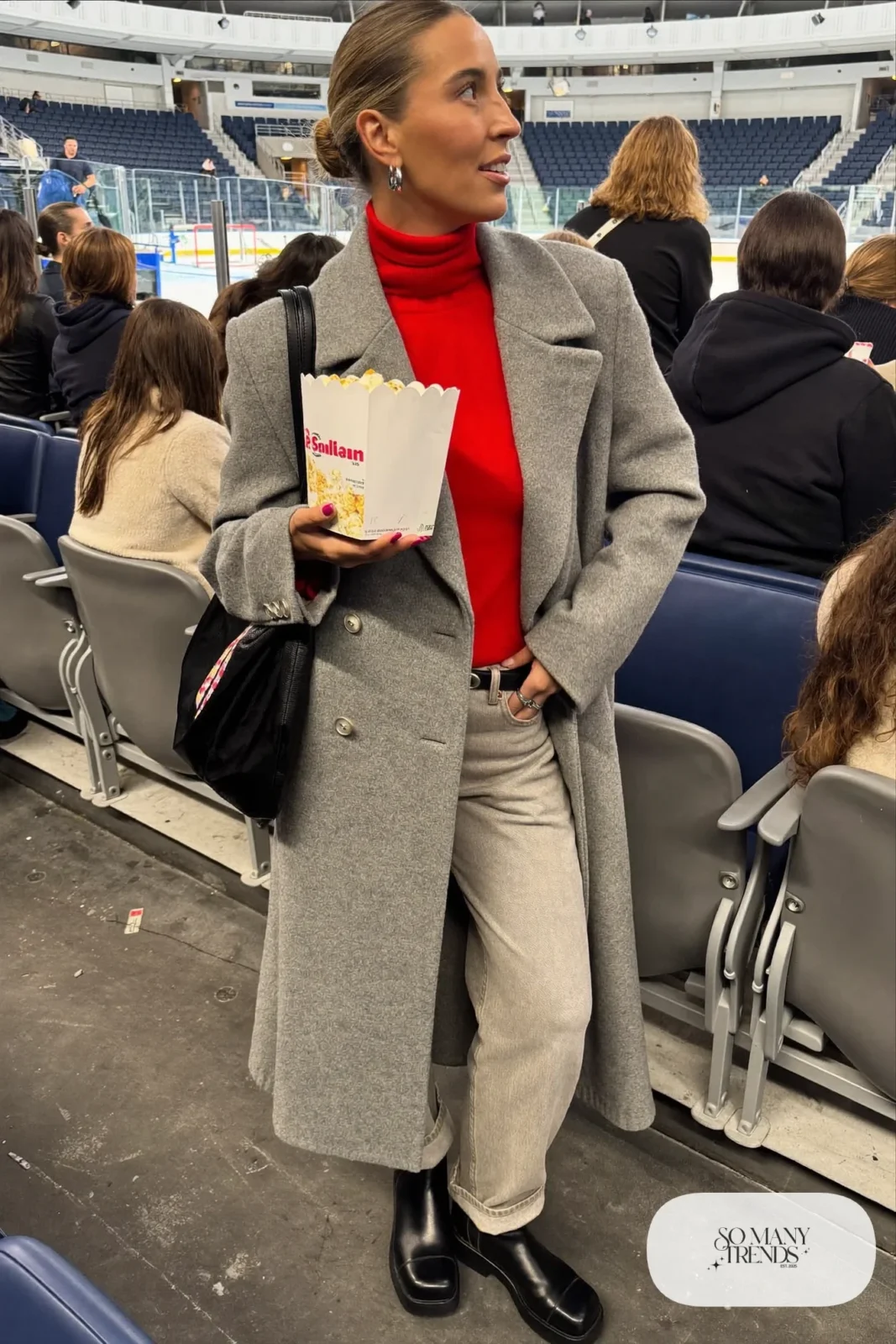 Woman in red turtleneck sweater, gray wide straight jeans, long gray double-breasted coat and black ankle boots, hockey game outfit 2