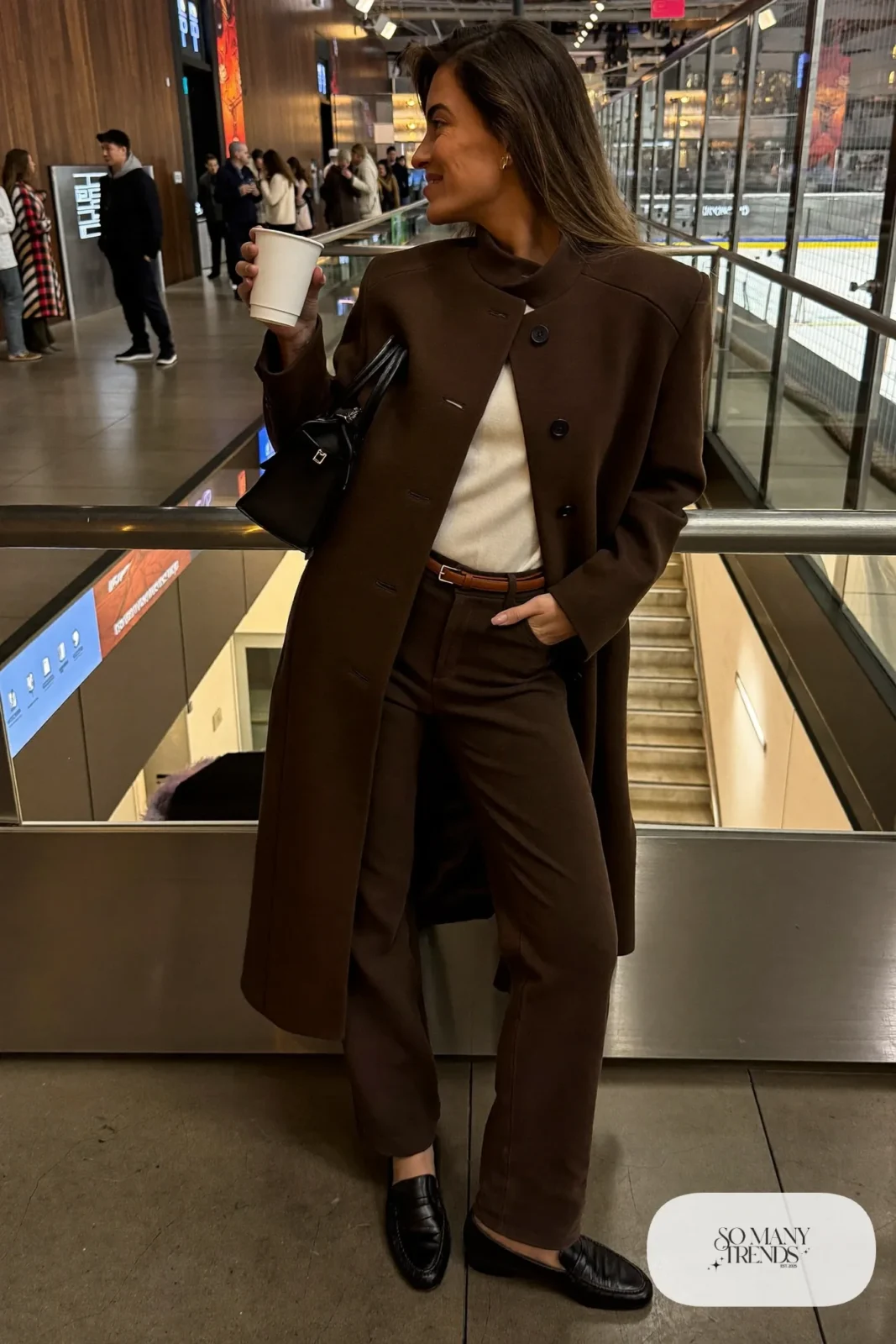 Woman in tailored espresso wool coat, cream knit sweater, brown straight pants and black leather loafers, hockey game outfit 5