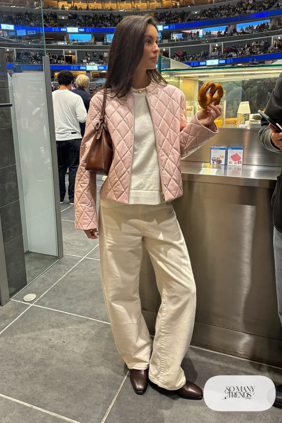 Woman in pale pink quilted jacket, cream knit sweater, cream wide-leg jeans and brown leather boots, hockey game outfit 10