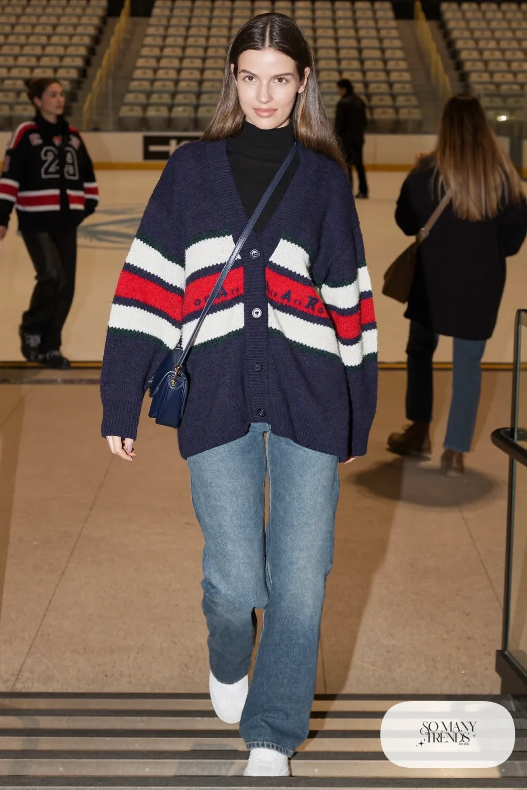 Woman in navy and cream varsity stripe cardigan, black turtleneck, straight jeans and white sneakers, hockey game outfit 11