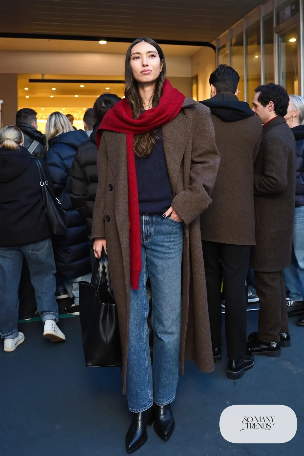 Woman in long oversized gray wool coat, navy ribbed sweater, straight blue jeans, red scarf and black boots, hockey game outfit 12