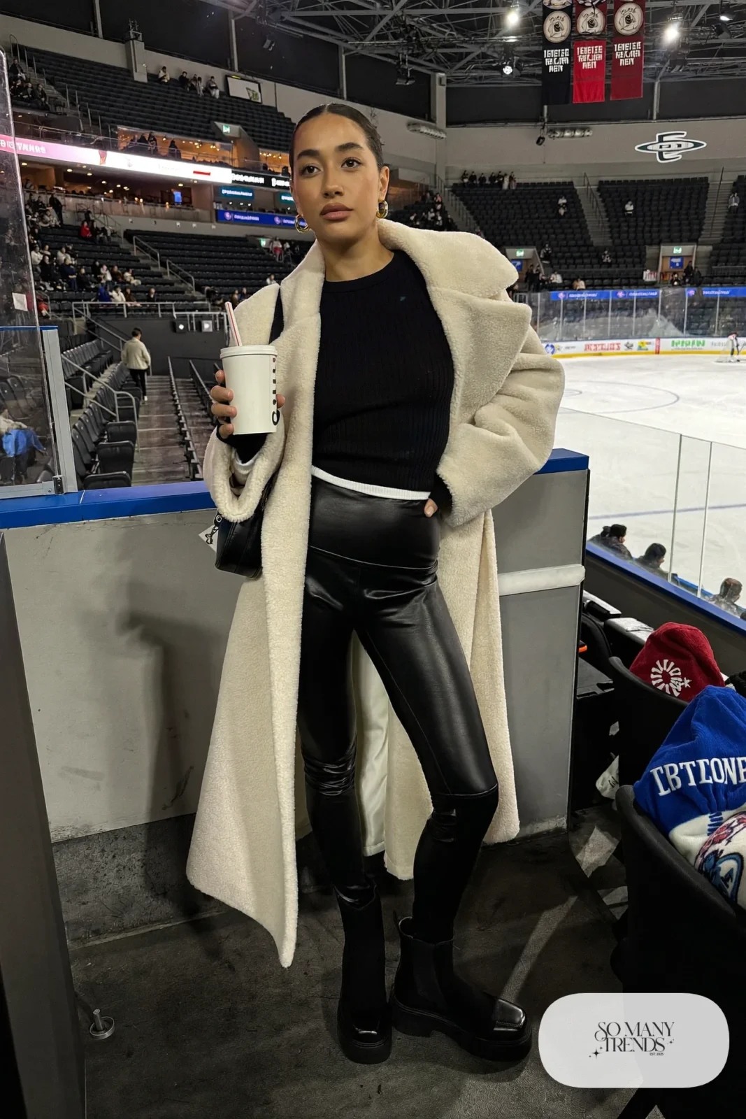 Woman in cream long teddy coat, black fitted sweater, black faux leather leggings and black ankle boots, hockey game outfit 13