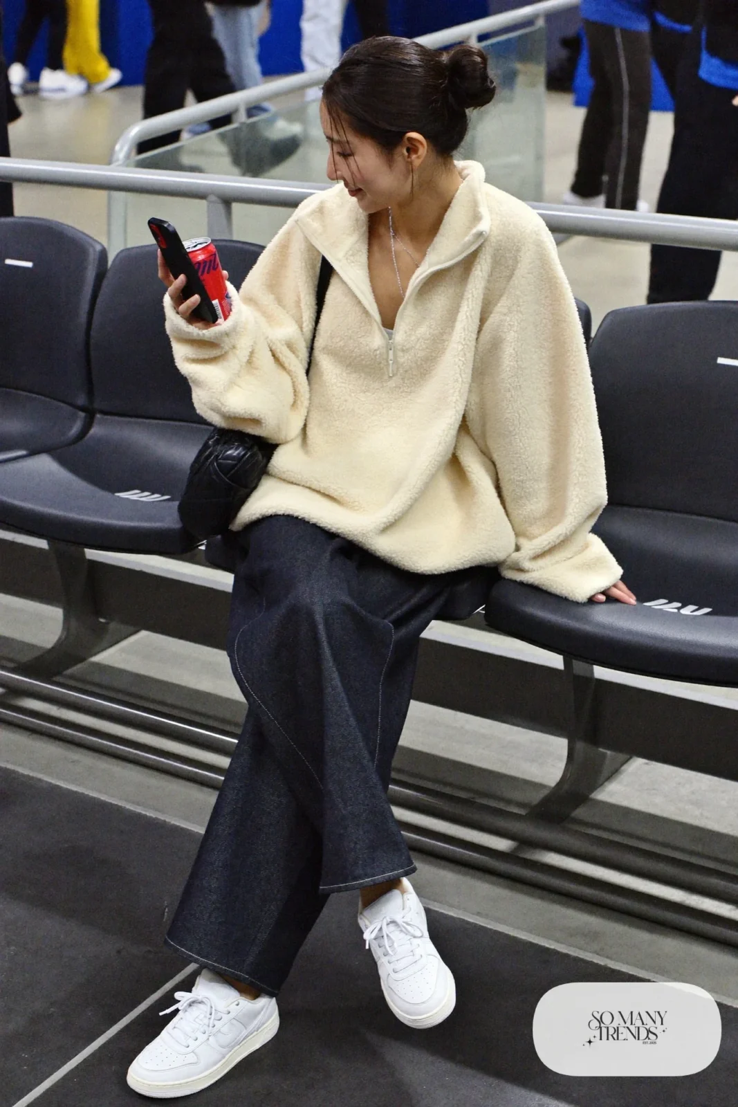 Woman in cream sherpa fleece pullover, dark barrel-leg jeans, white sneakers and black crossbody bag, hockey game outfit 17