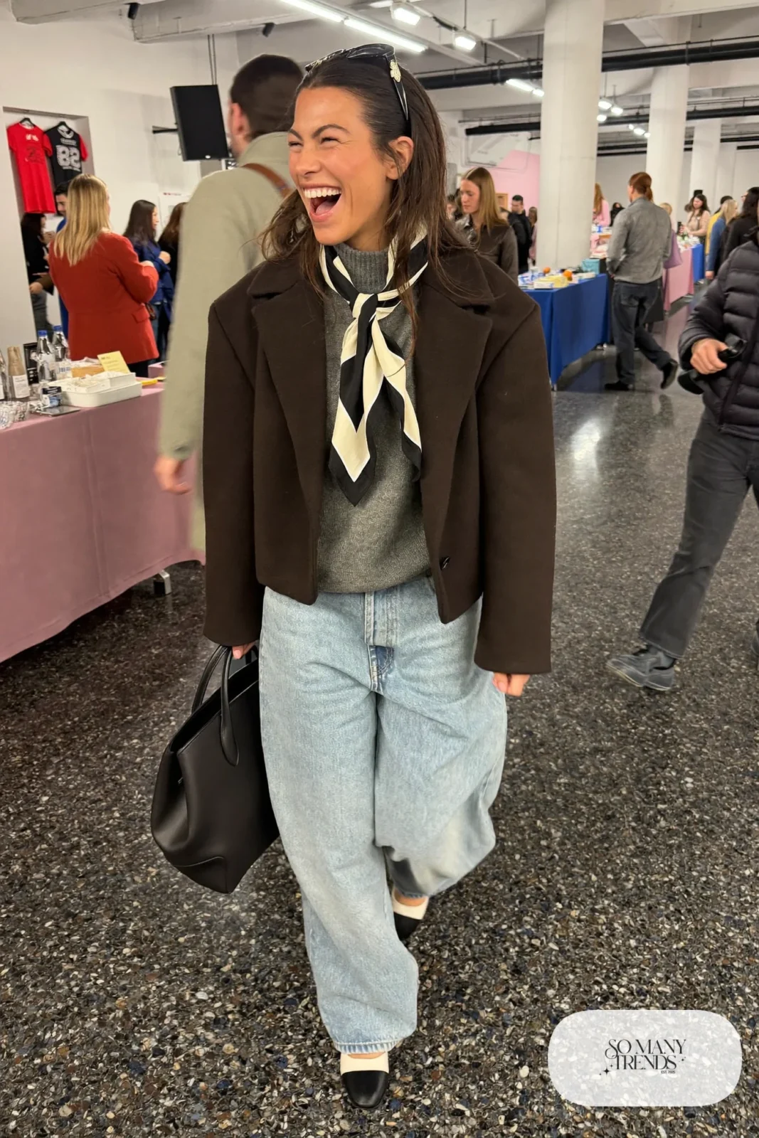 Woman in short black wool jacket, printed scarf, light-wash baggy jeans, gray knit and black flats, hockey game outfit 23