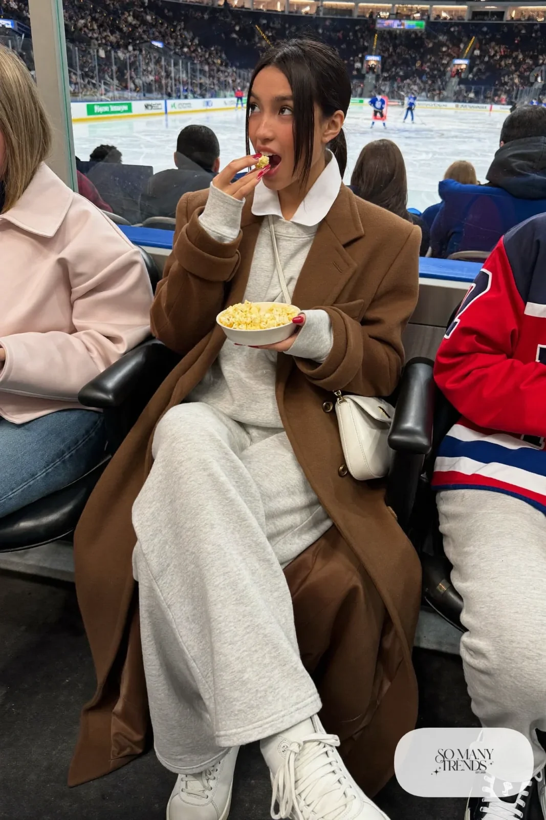 Woman in heavyweight gray sweatsuit set, pale pink beanie, long camel coat and white sneakers, hockey game outfit 26