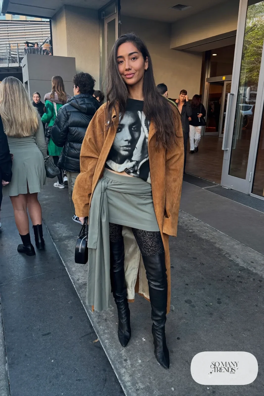 Woman in a boxy black graphic tee, gray mini skirt with sash, lace tights, over-the-knee boots and camel suede shirt-coat, basketball game outfit 8