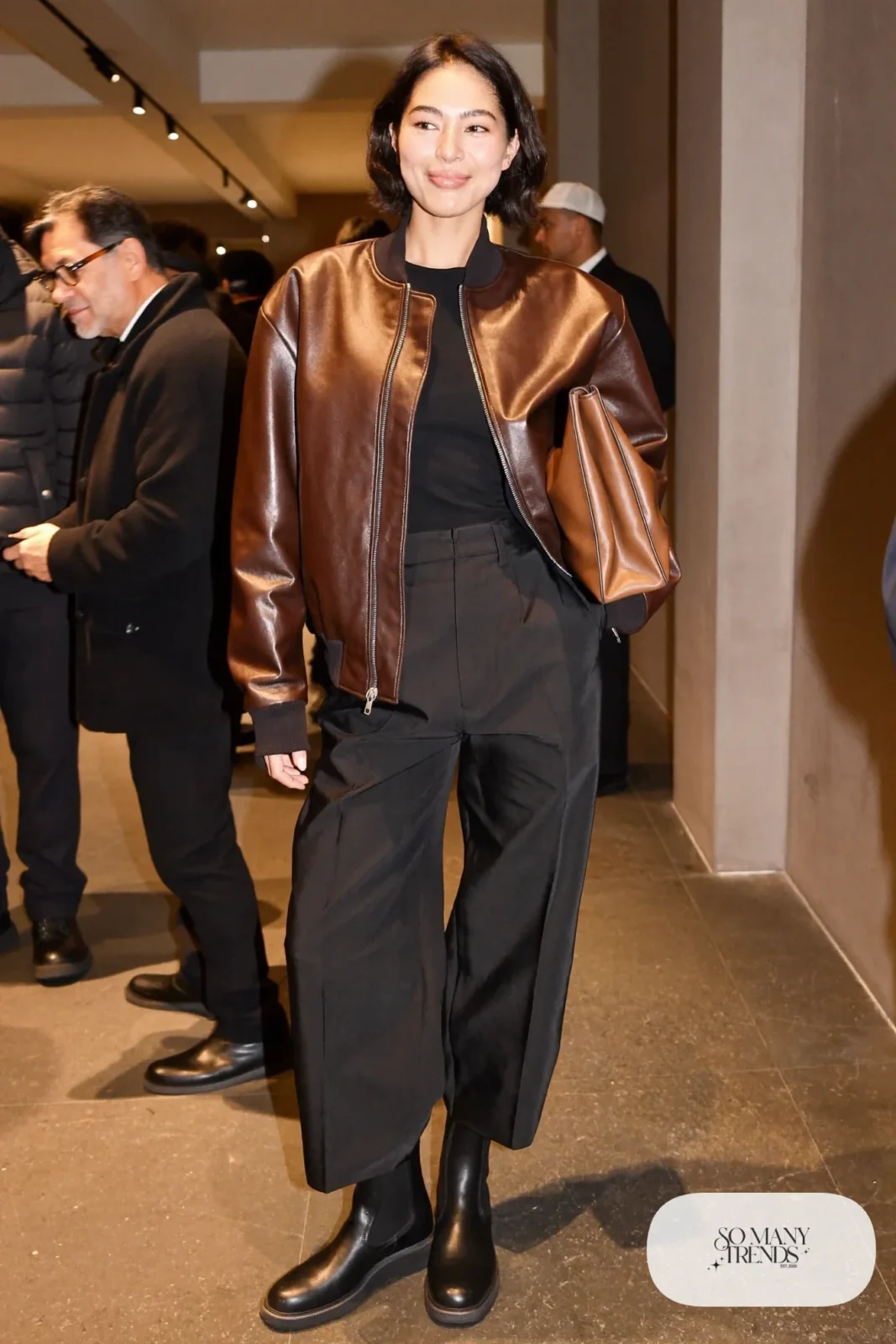 Woman in a brown leather bomber, black top, black wide pants and chelsea boots with a cognac clutch, basketball game outfit 9