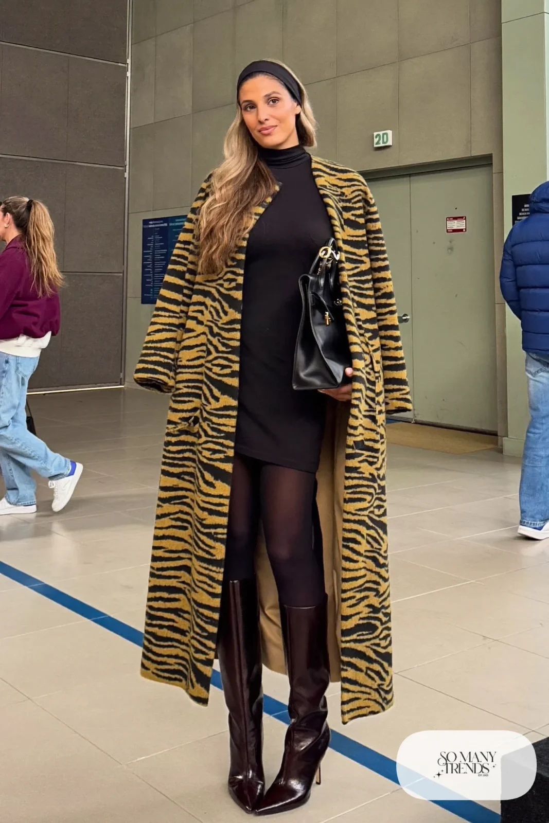 Woman in a black and ochre tiger-stripe knit dress over a long-sleeve black tee with dark boots and structured bag, basketball game outfit 11