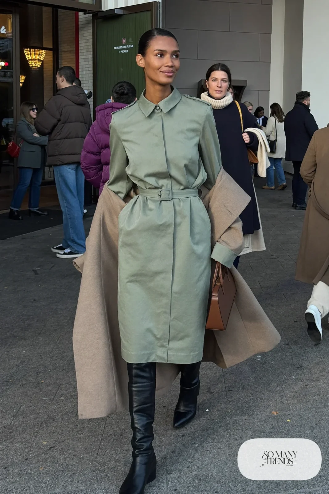 Woman in a sage belted shirt dress, long camel coat and black knee-high boots, basketball game outfit 14