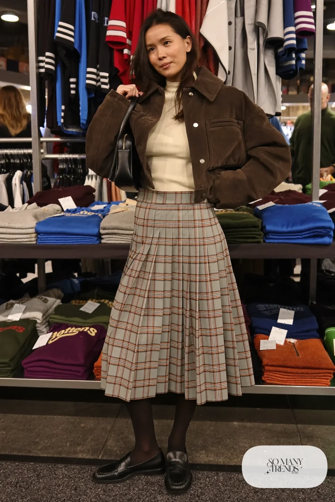 Woman in a sage and brown plaid pleated skirt, ribbed turtleneck, cropped quilted jacket, black tights and loafers, basketball game outfit 16