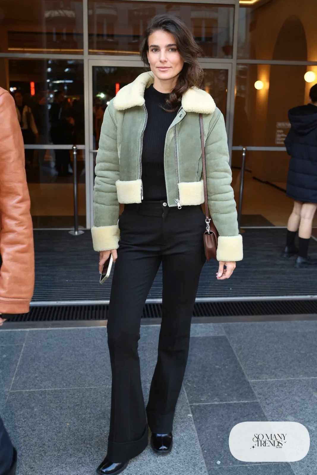Woman in an oatmeal cropped shearling jacket, black ribbed knit, flared black pants and ankle boots, basketball game outfit 18