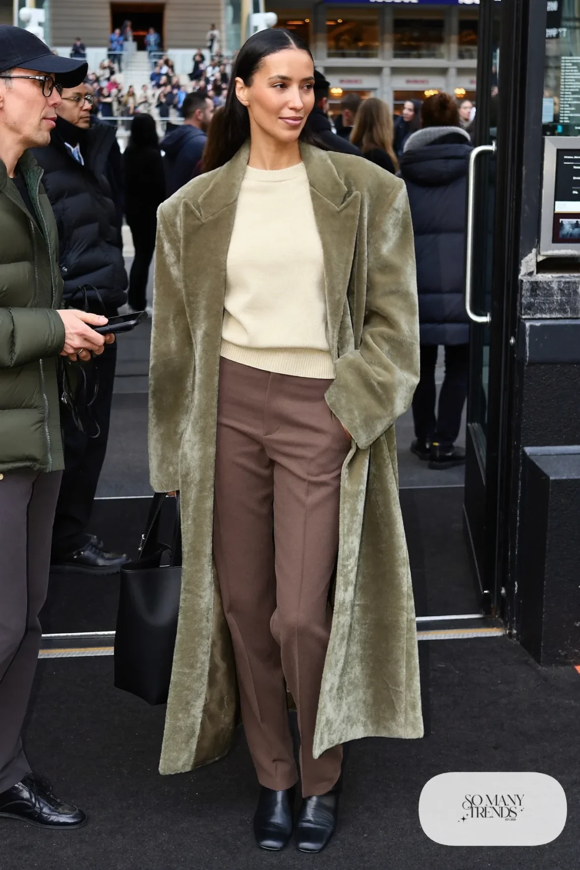 Woman in a long sage wool coat, oatmeal knit tee, straight espresso pants and black boots, basketball game outfit 19