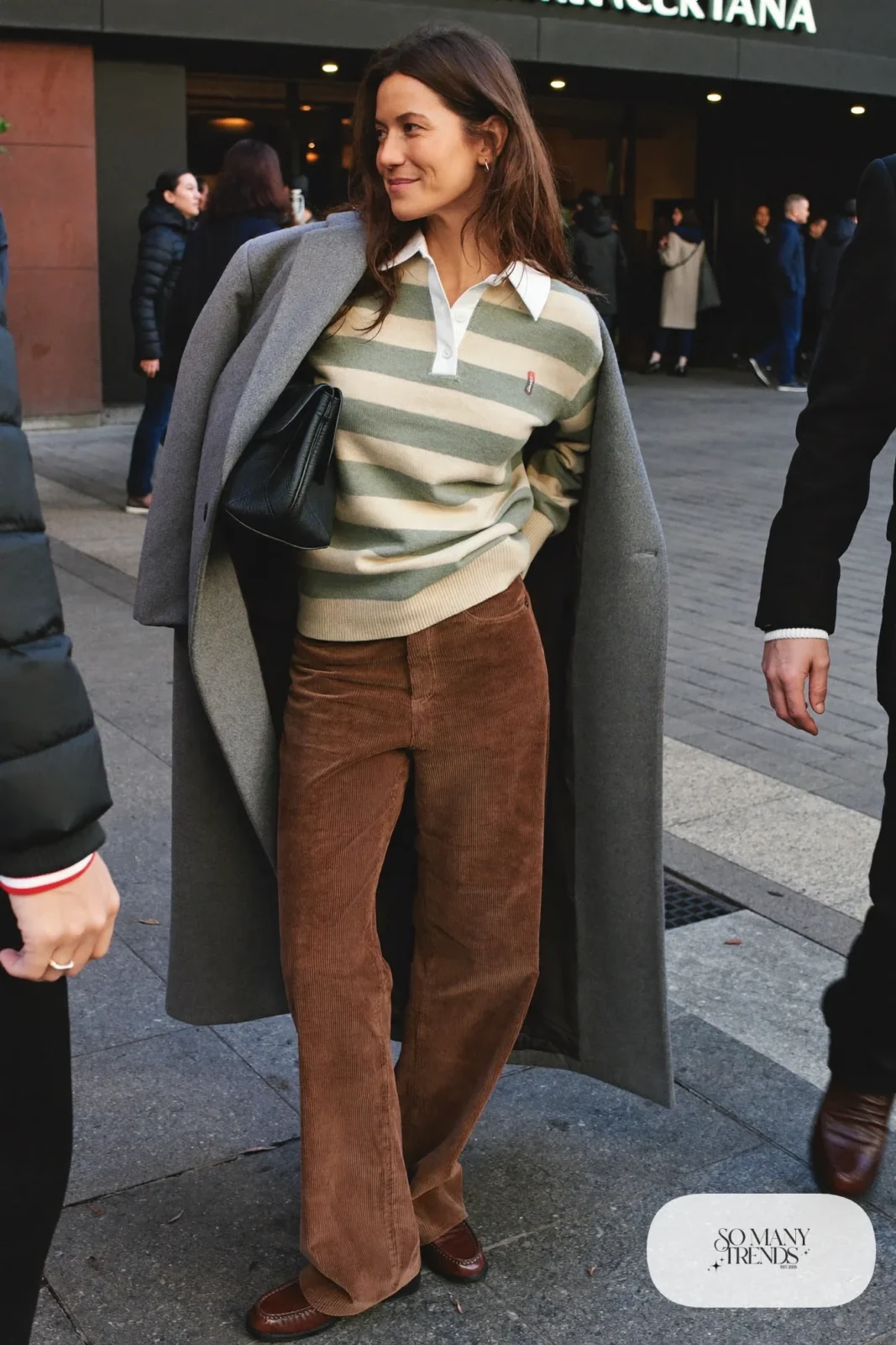 Woman in wide espresso corduroy pants, sage and oatmeal rugby sweater, brown loafers and wool coat, basketball game outfit 25