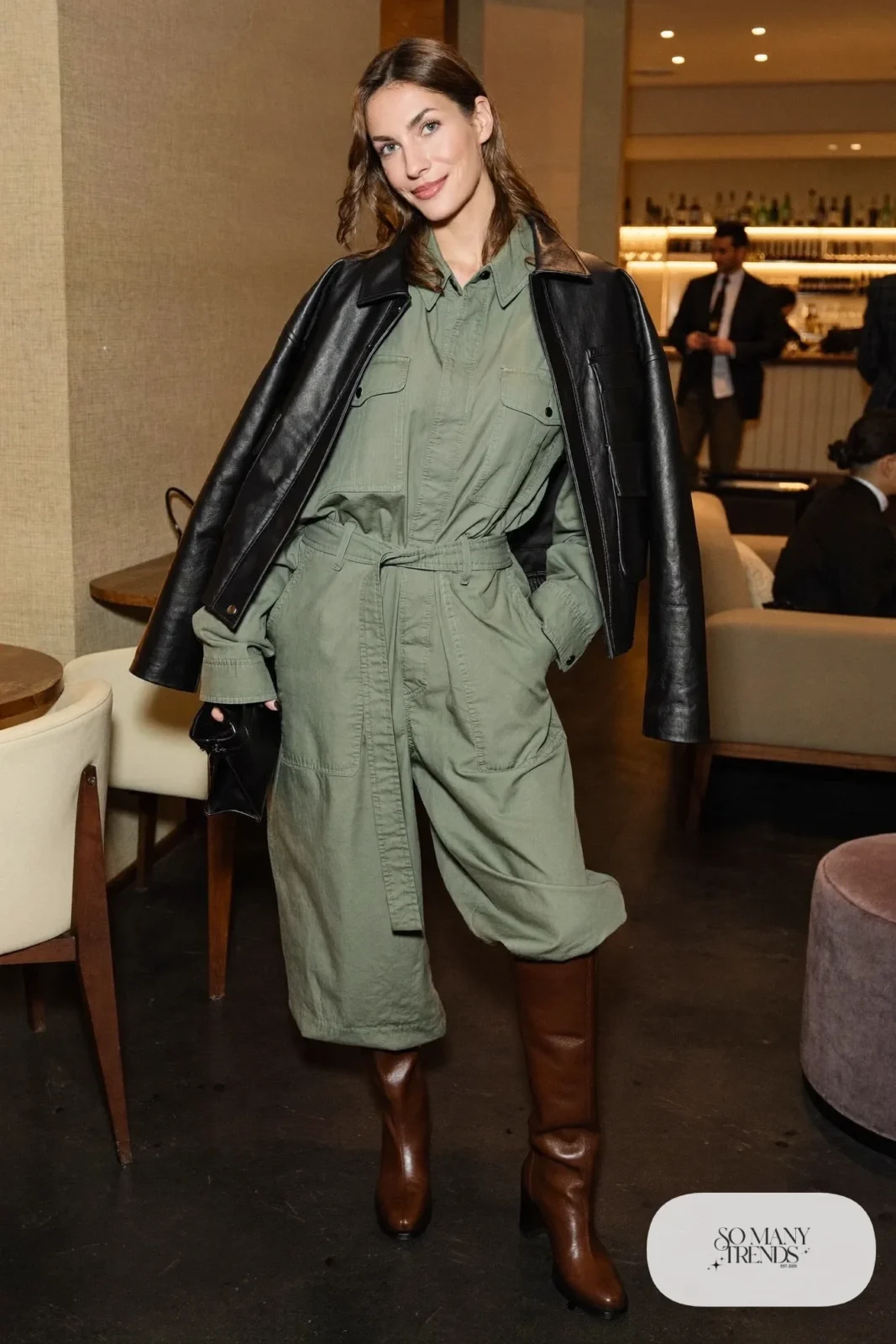 Woman in a sage utility jumpsuit, black leather jacket and brown boots, basketball game outfit 27