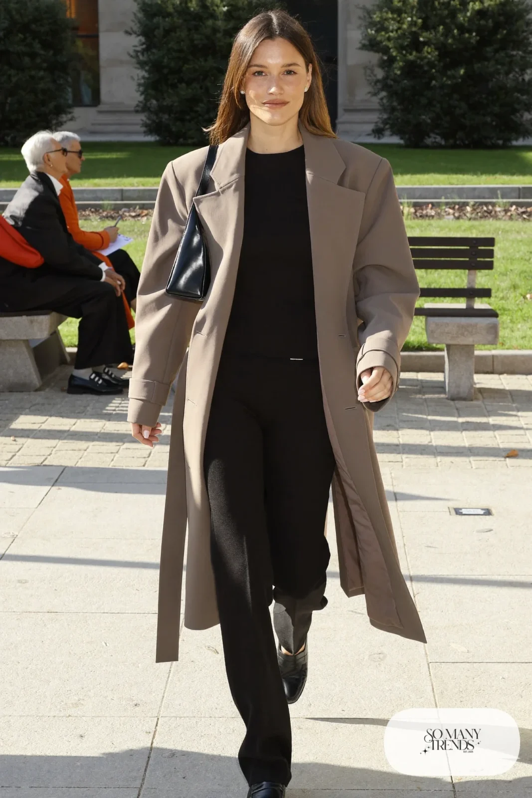 taupe long trench coat over black knit top and matching knit pants with black loafers, interview outfit 21