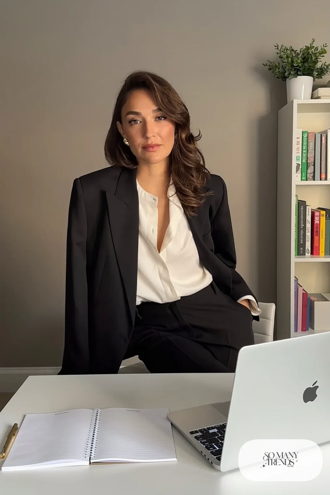 ivory blouse under black blazer seated at a desk for a video interview with small gold studs, interview outfit 23