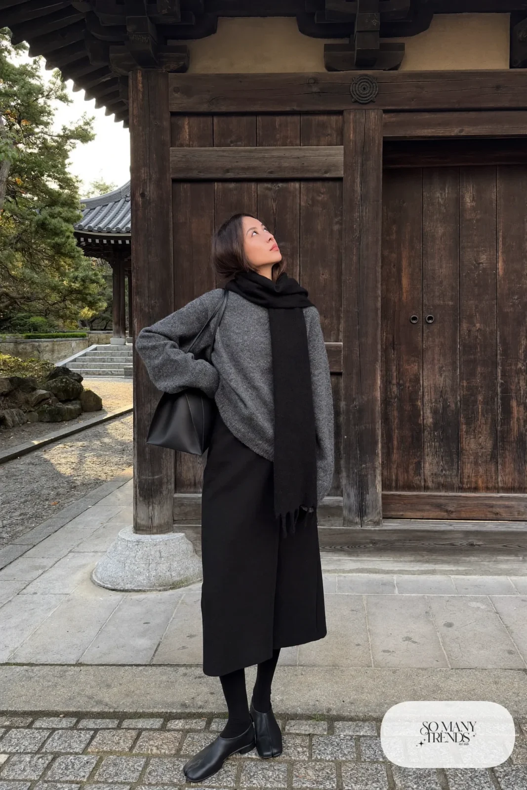 Woman in a charcoal chunky knit sweater, long black wool skirt, black opaque tights and flat leather boots near a Kyoto temple gate, outfit 3