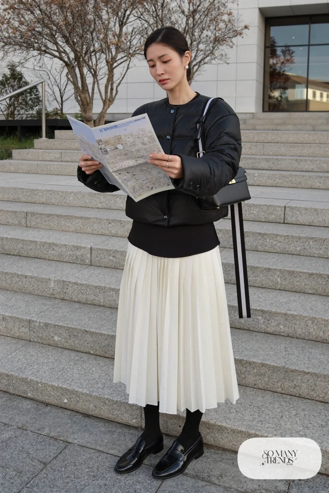 Woman in a black cropped quilted jacket, pearl pleated midi skirt, black opaque tights and black loafers near a Tokyo museum, outfit 17