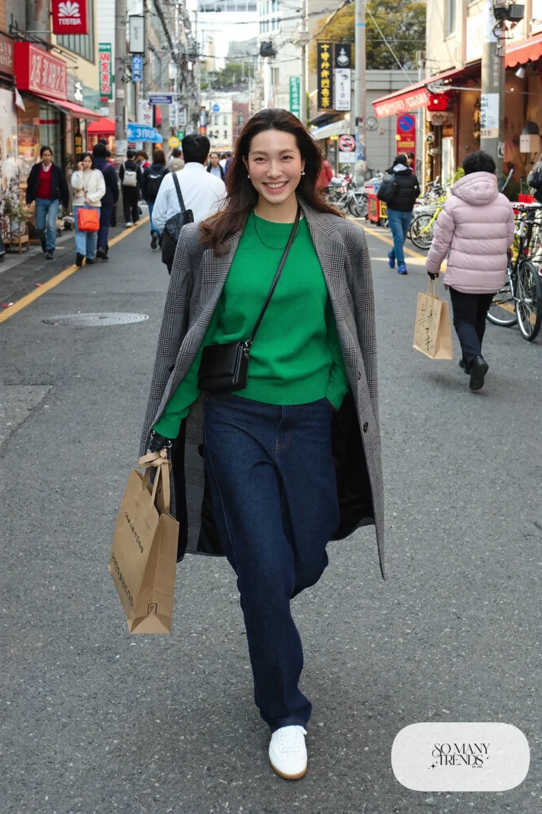 Woman in an oversized gray check wool coat, emerald crewneck sweater, dark straight jeans and white leather sneakers on a Tokyo street, outfit 21