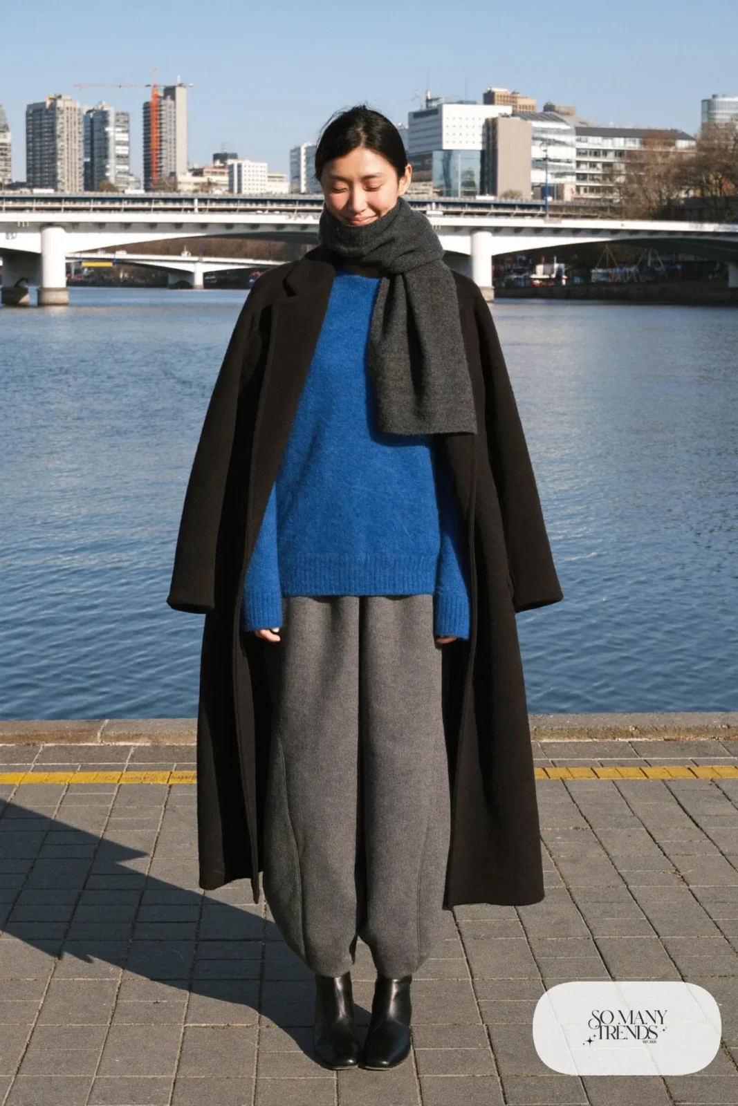 Woman in a cobalt blue sweater, gray flannel barrel pants, long black coat and black leather boots in Tokyo, outfit 23