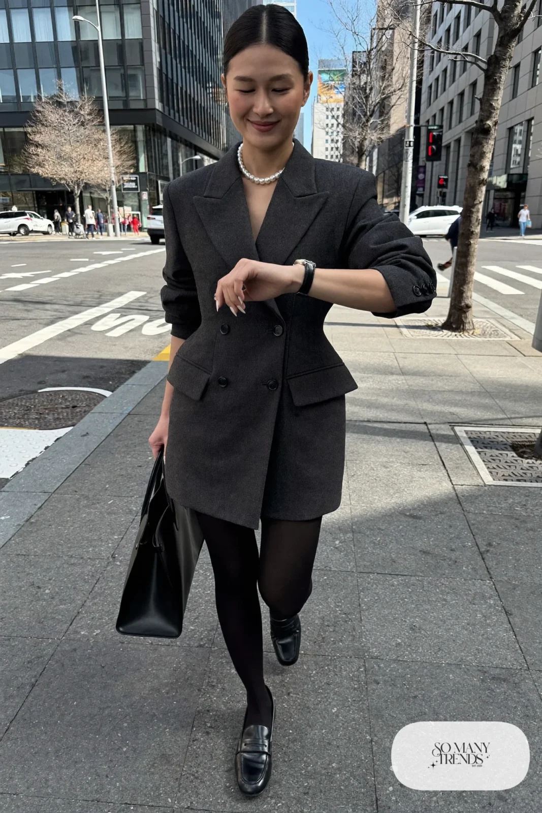 Woman in a charcoal wool blazer dress with black opaque tights, black loafers and a pearl necklace in a Tokyo business district, outfit 26