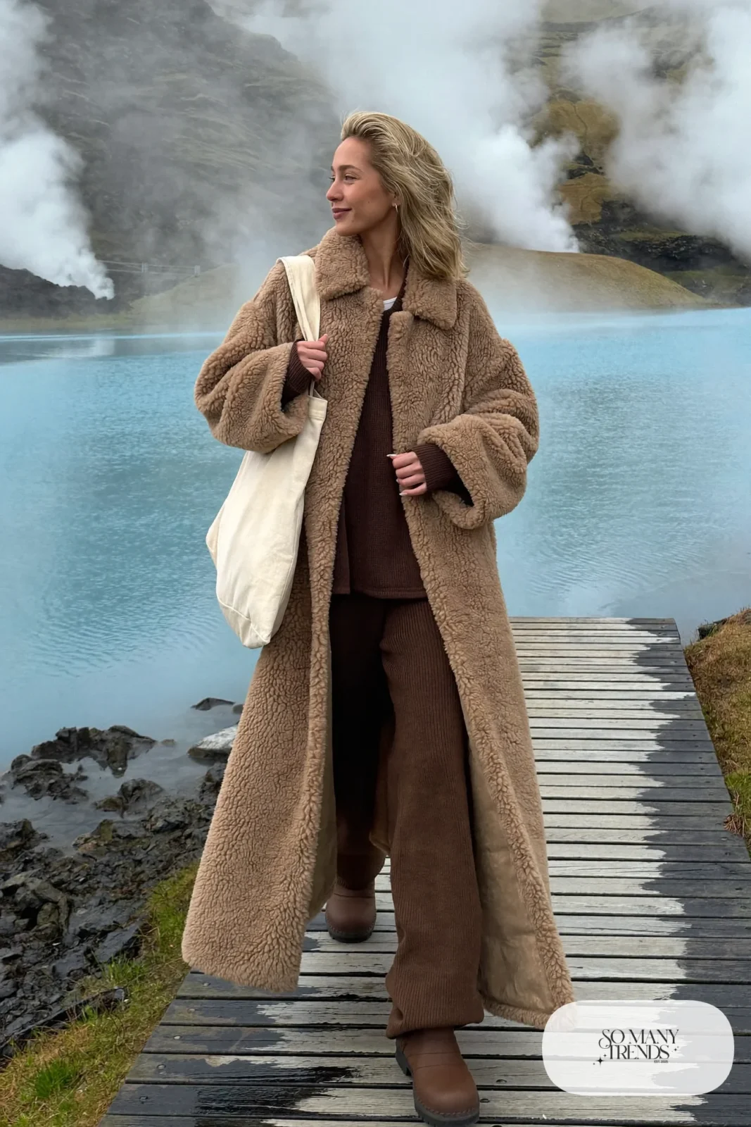 Woman in a long camel teddy coat, brown knit set, waterproof boots and tote bag near a geothermal lagoon, outfit 14