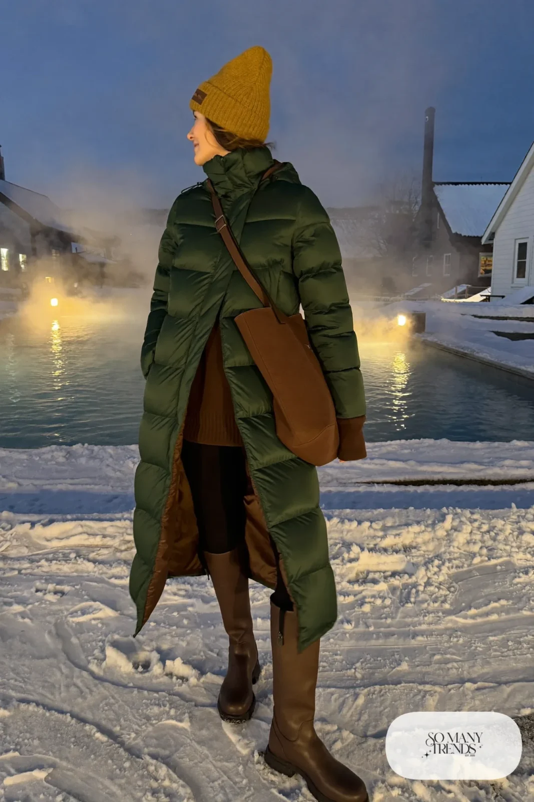 Woman in a long forest green puffer coat, brown boots, wool hat and tote walking to a geothermal pool, outfit 17