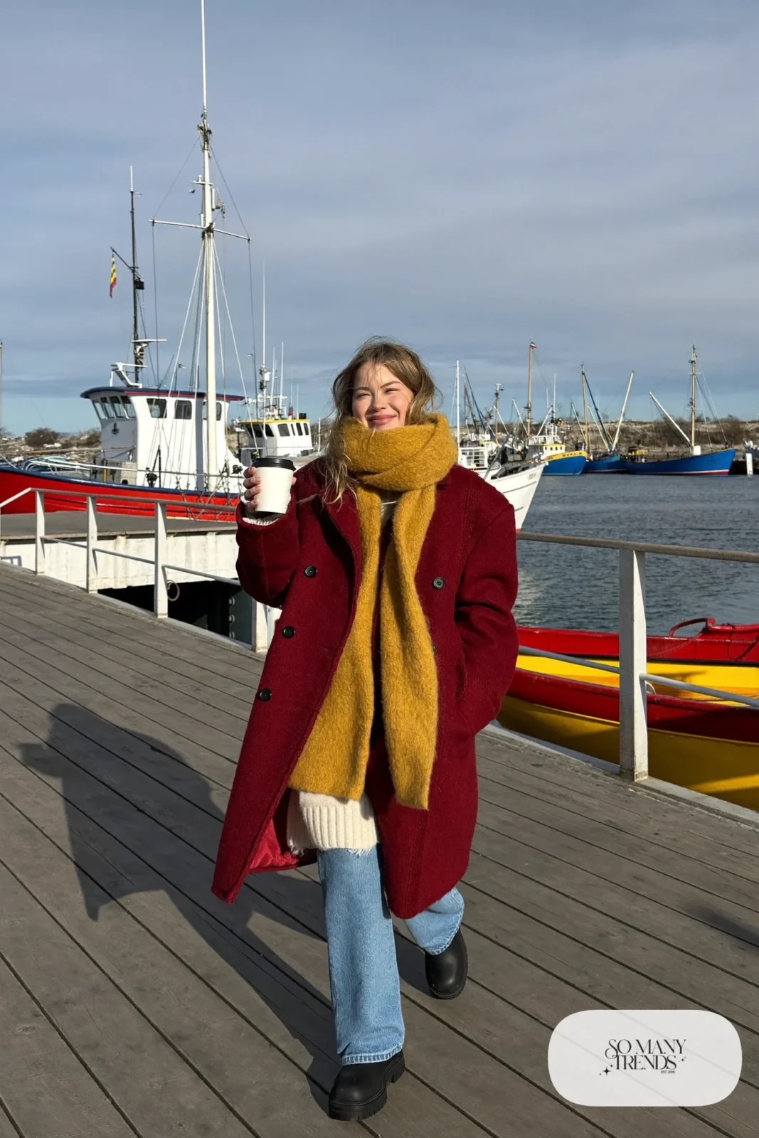 Woman in a burgundy wool pea coat, cream sweater, straight blue jeans and lug-sole boots at Reykjavik harbor, outfit 19