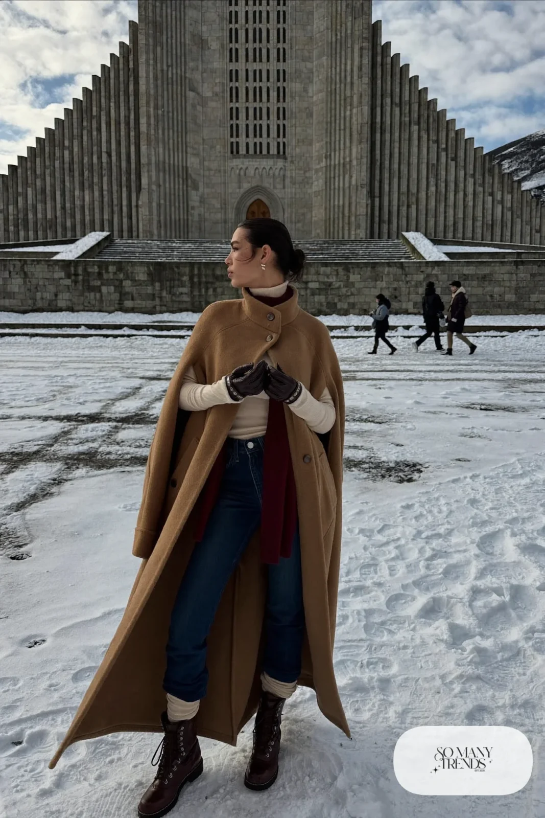 Woman in a camel cape coat, cream turtleneck, slim dark pants and brown boots near Hallgrimskirkja, outfit 20